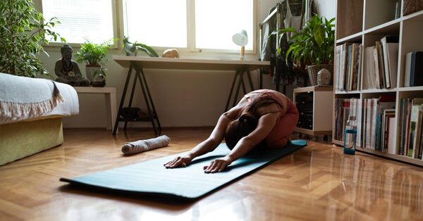 阳光照进房间，一位成年人在垫子上做温和的拉伸动作，氛围柔和